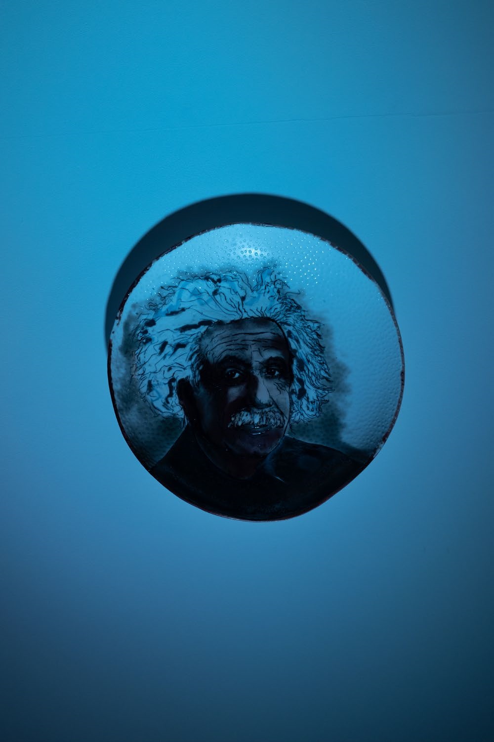 Einstein in blue curiously looking out of a blue wall.