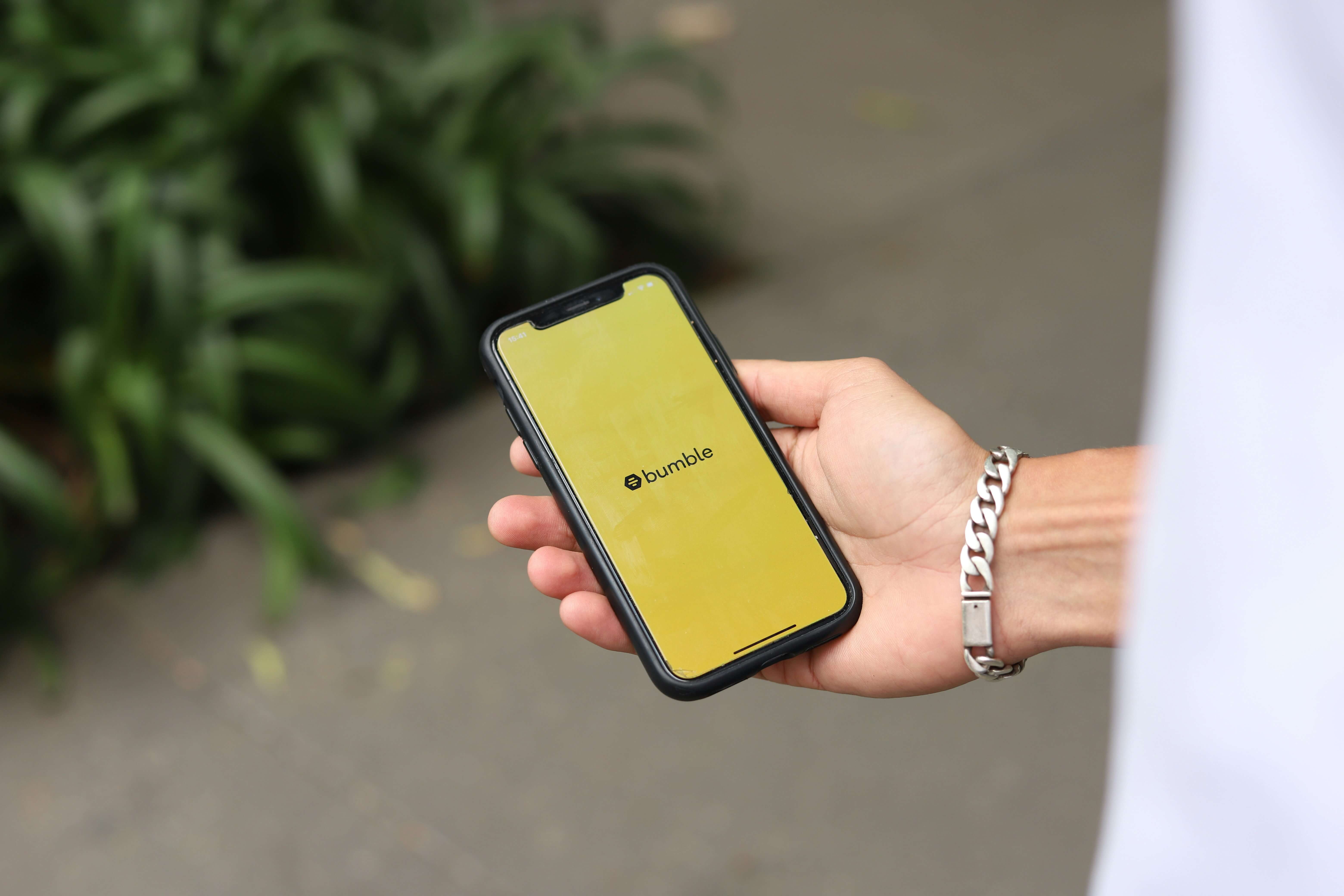 A hand holding a phone with the Bumble dating app on it.