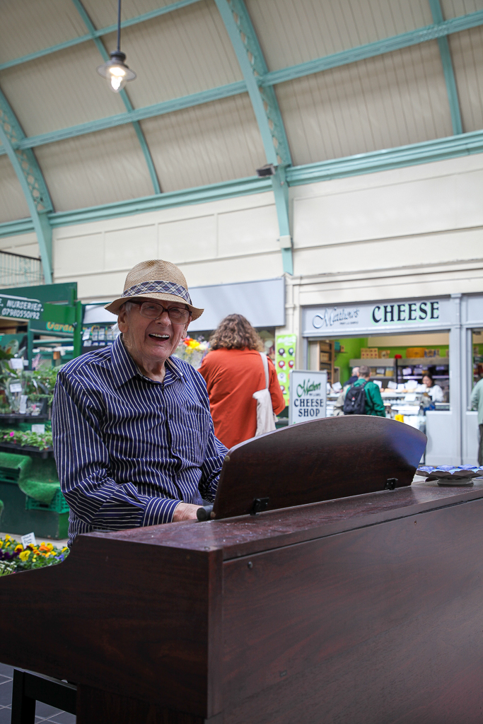 Older man playing the piano in Grainger Market smiling