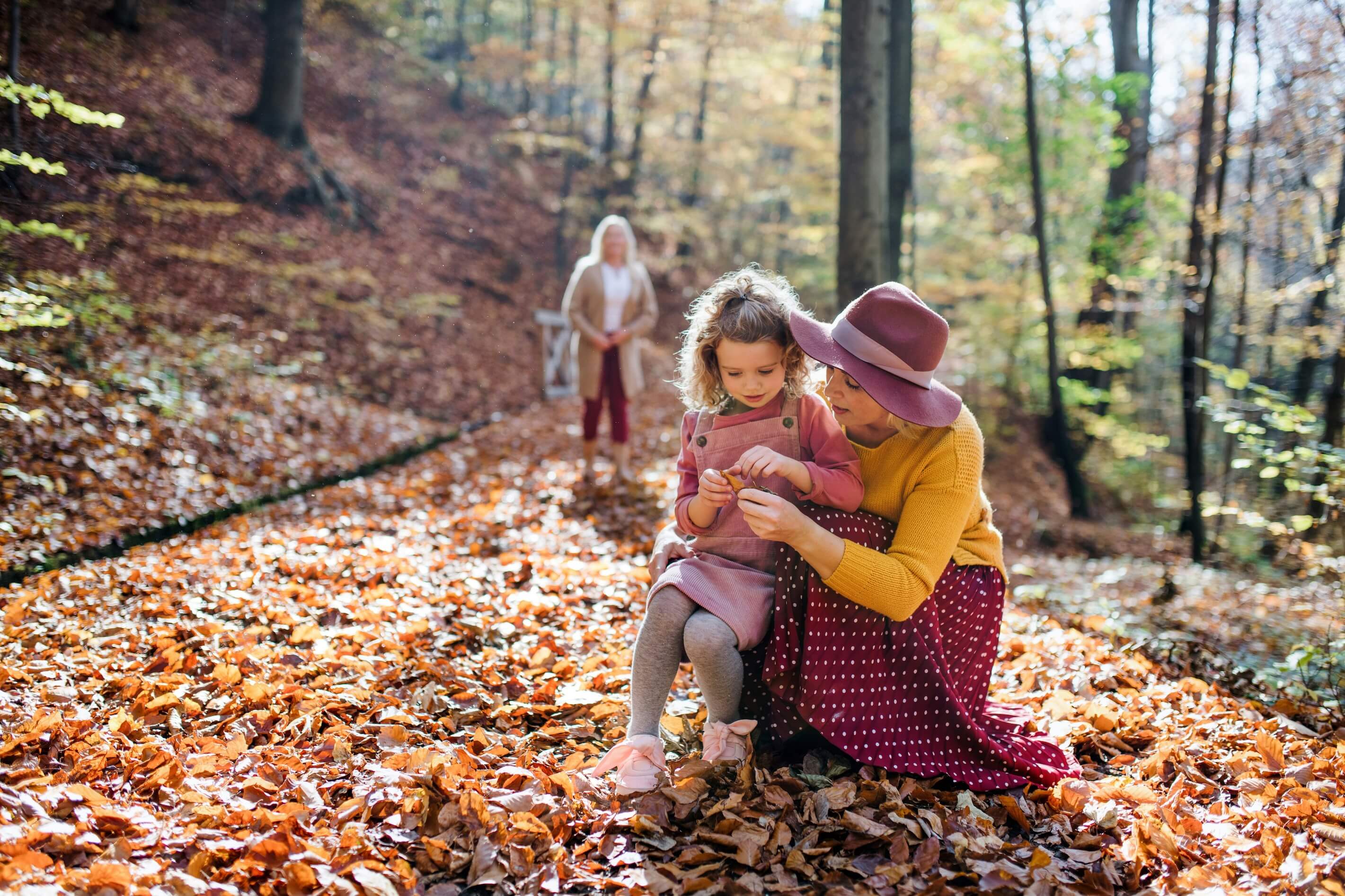 Young girl with mother and grandmother playing in Autumn leaves