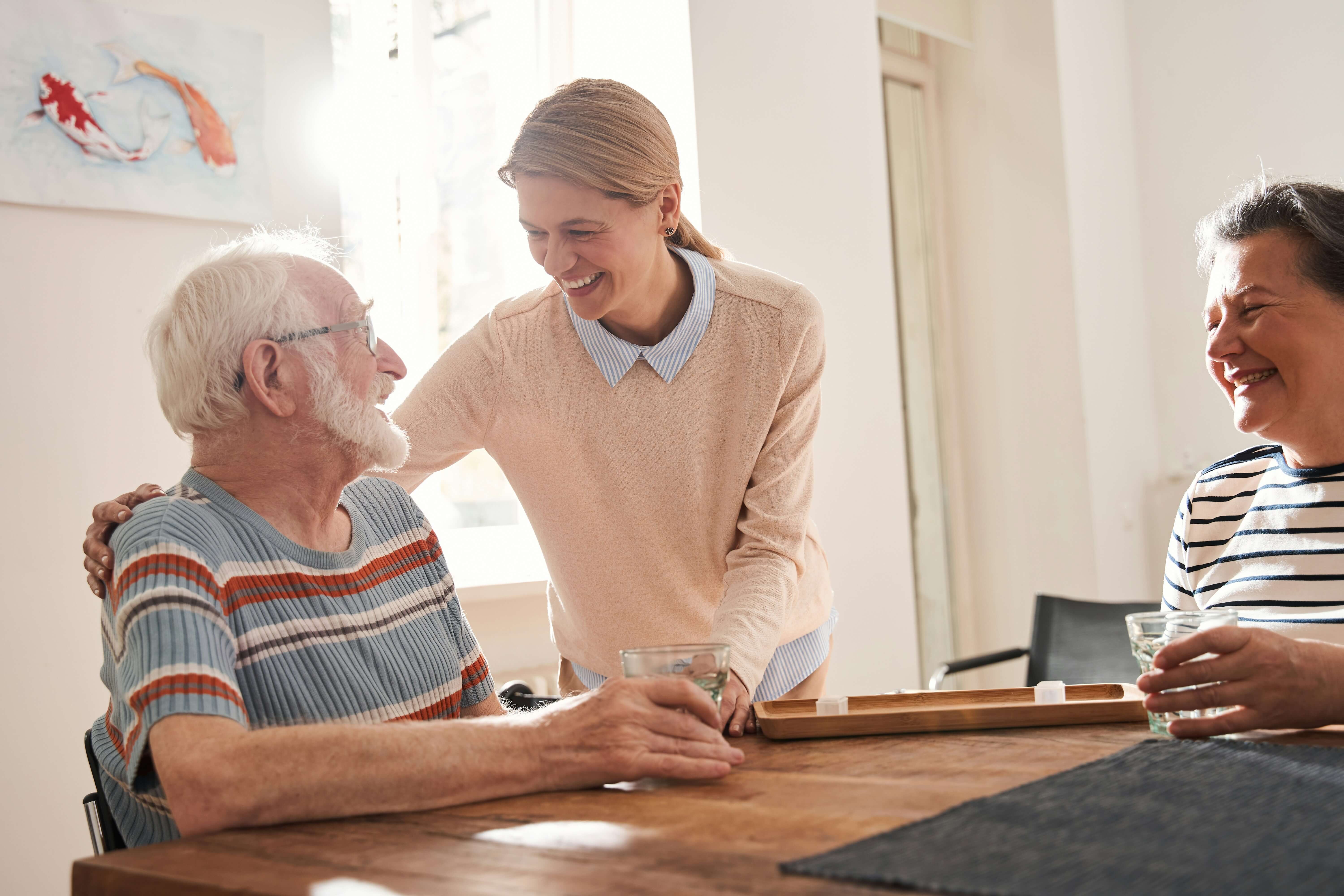 Carer putting arm around an older man around a kitchen table