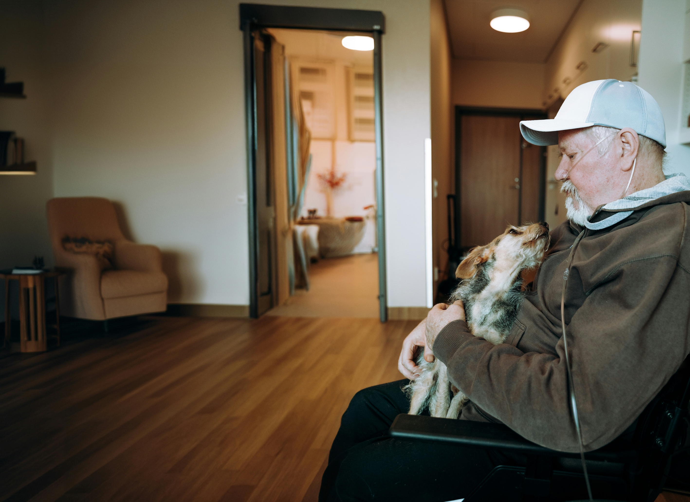 Man in a wheelchair with oxygen mask cuddling a dog