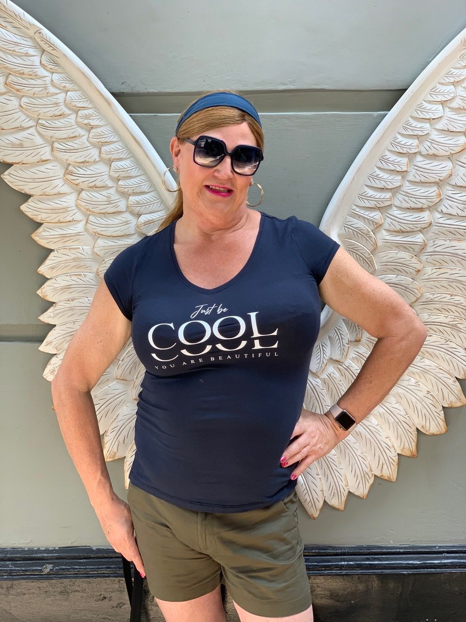 Cynthia, wearing a t shirts and shorts in front of angel wings.