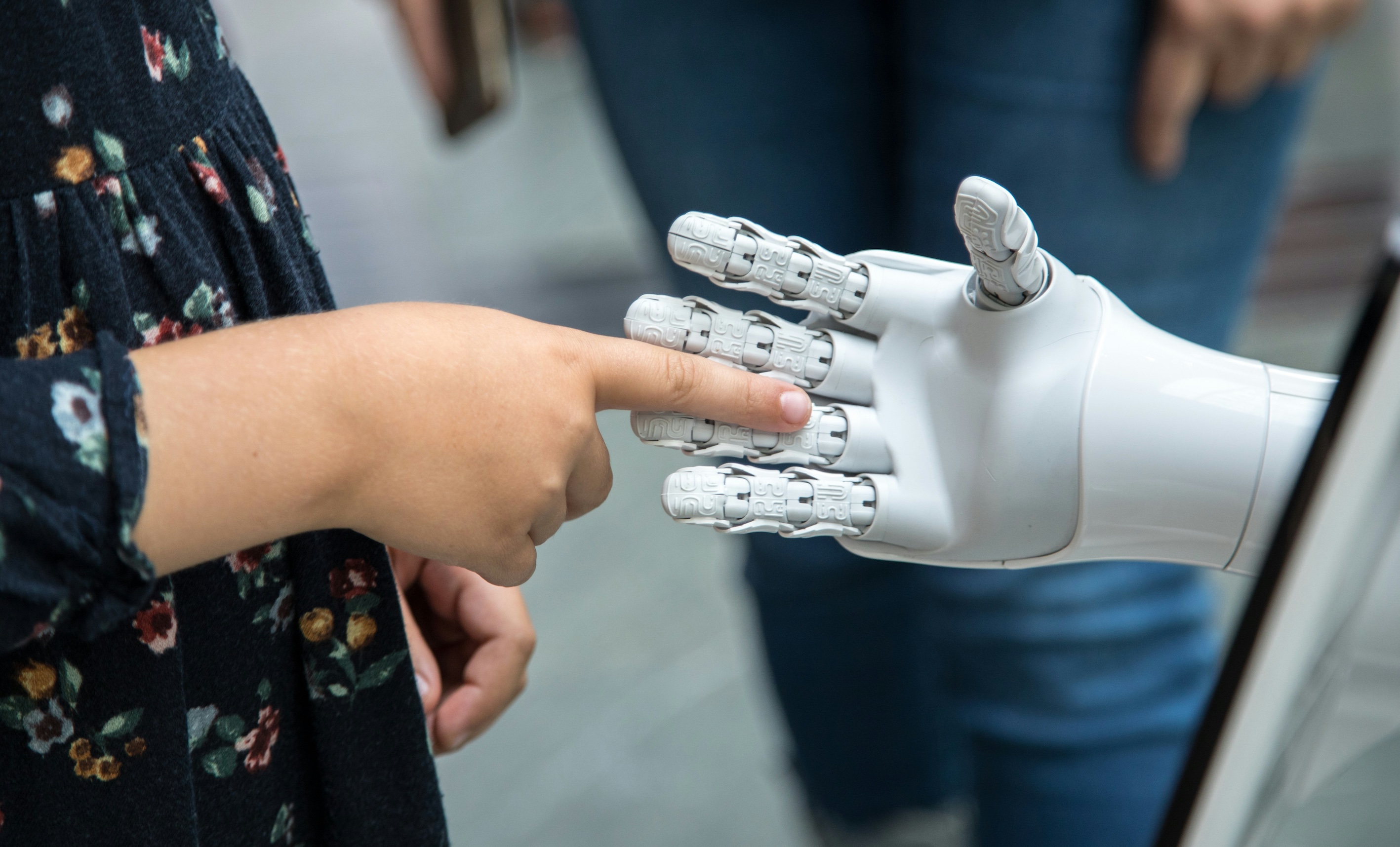 A young girl touching a robots hand with her finger