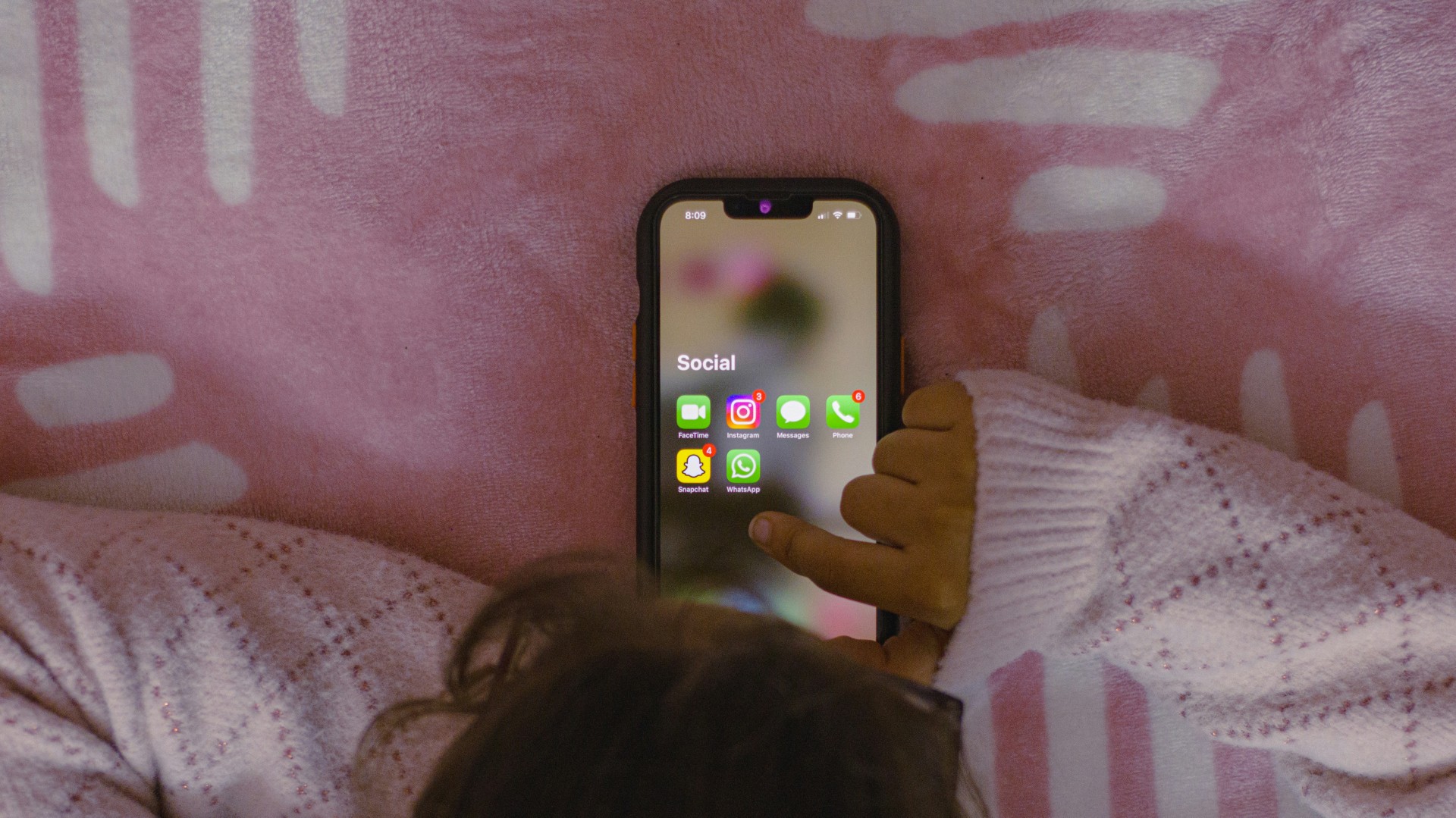 Someone looking at their phone on a pink bed spread